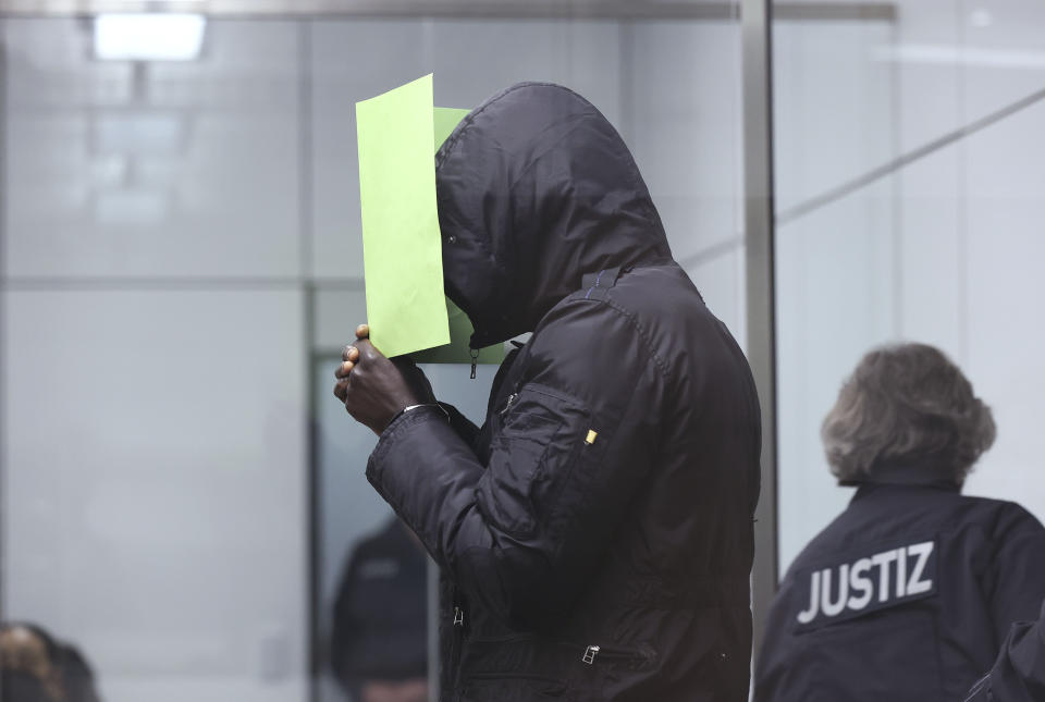 The Gambian defendant, identified only as Bai L. in line with German privacy rules, holds a folder in front of his face at the Celle Higher Regional Cour in Celle, Germany, Monday, April 25, 2022. The man went on trial in Germany on Monday for his alleged role in the killing of government critics in the West African country over 15 years ago. (Ronny Hartmann/Pool Photo via AP)