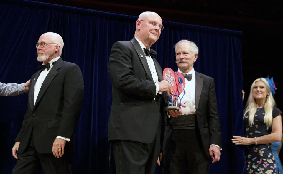 John Barrett, center, holds his Ig Nobel award with fellow recipients Bruce Blank, right, and Michel Boileau, left, during ceremonies at Harvard University in Cambridge, Mass., Thursday, Sept. 13, 2018. The men won for using postage stamps to test whether the male sexual organ is functioning properly. (AP Photo/Michael Dwyer)
