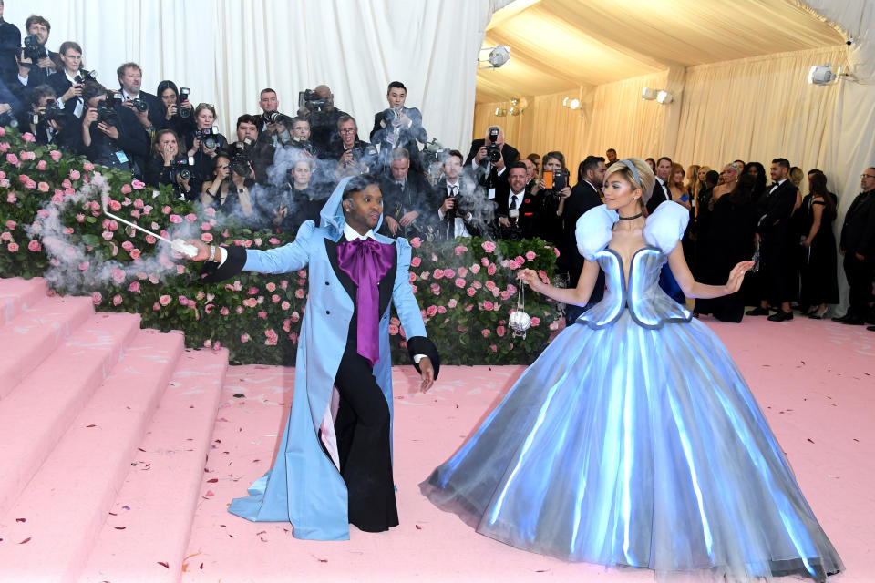 Law dress as the Fairy Godmother waving a smoke-emitting wand at Zendaya who is wearing a Cinderella-esque gown on the steps of the Met Gala