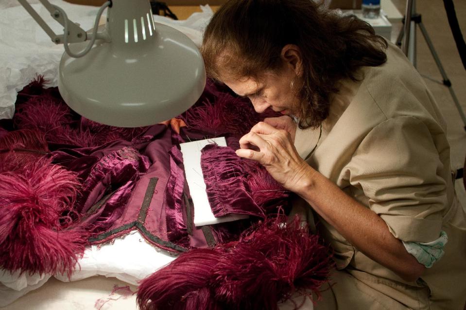In this undated photo provided by the Harry Ransom Center, conservator Cara Varnell works on the burgundy ball gown from "Gone With The Wind." Varnell determined that some feathers were original and some were replacements. The ball gown as well as the iconic green curtain dress from the 1939 film were saved from deterioration by a $30,000 conservation effort by the Harry Ransom Center at the University of Texas, and are on display for the first time in nearly 30 years at London's Victoria and Albert Museum as part of a Hollywood costume exhibit. (AP Photo/Harry Ransom Center)