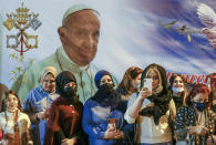 Women wait outside the Chaldean Cathedral of Saint Joseph, in Baghdad, Iraq, Saturday, March 6, 2021, where Pope Francis, depicted on a giant poster at their back, is concelebrating a mass. Earlier today Francis met privately with the country's revered Shiite leader, Grand Ayatollah Ali al-Sistani. (AP Photo/Andrew Medichini)