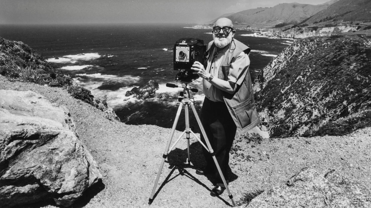  Photographer Ansel Adams stands with a large format camera on a tripod while photographing the Big Sur Coast near Carmel, California. |. 