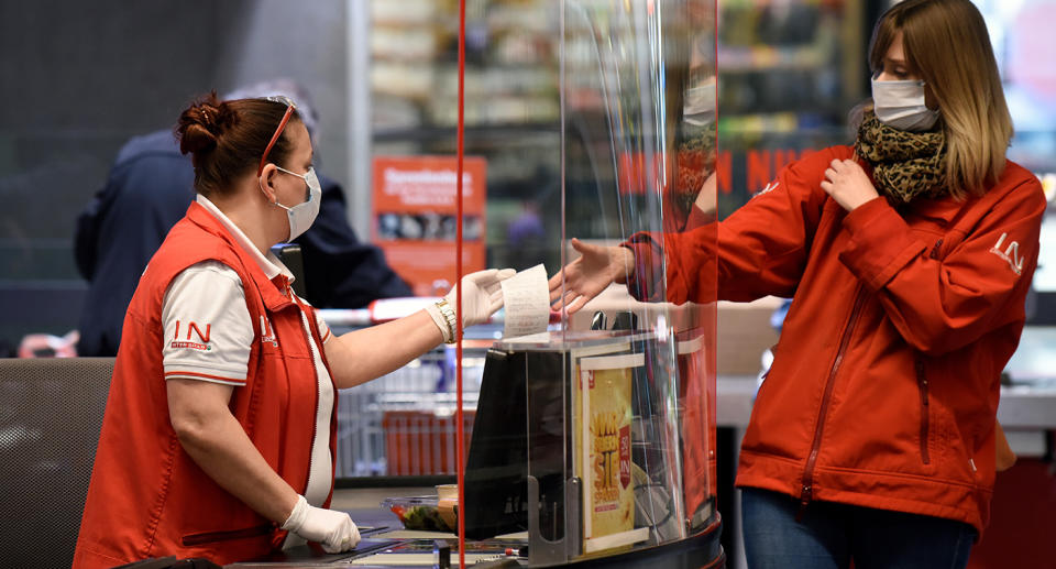 Supermarket staff wearing gloves and a face mask hands a receipt to a shopper also wearing a mask in Austria.