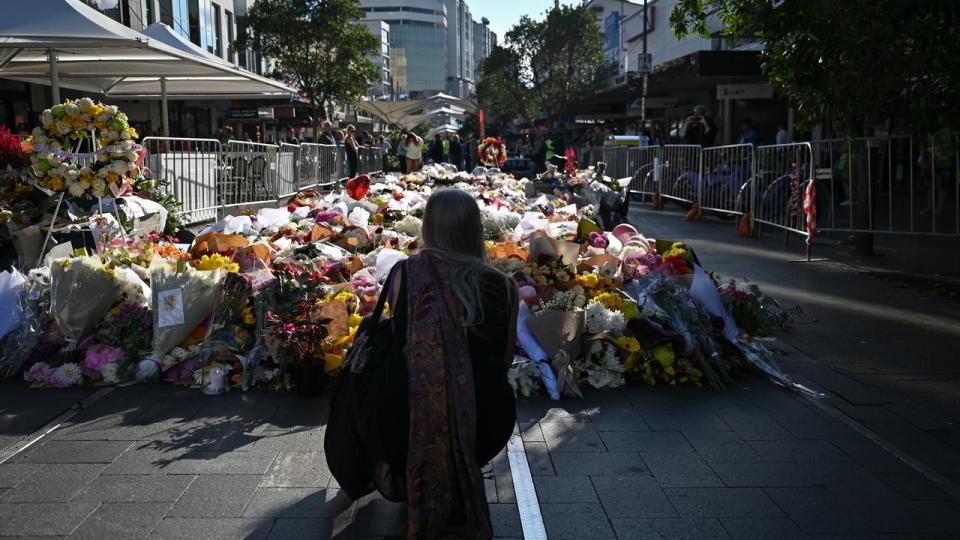 Woman kneels in front of floral tributes