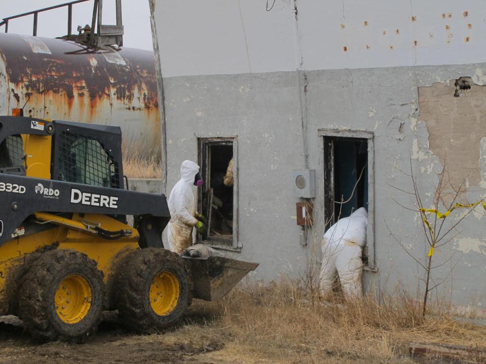 In this photo taken on Wednesday, April 23, 2014, white-suited workers wearing respirators clean up the illegal filter sock dump in an abandoned gas station in Noonan, N.D., near the Canadian border. Radiological readings were to be conducted to be sure the building and soil was back to normal. (AP Photo/The Bismarck Tribune, Lauren Donovan)