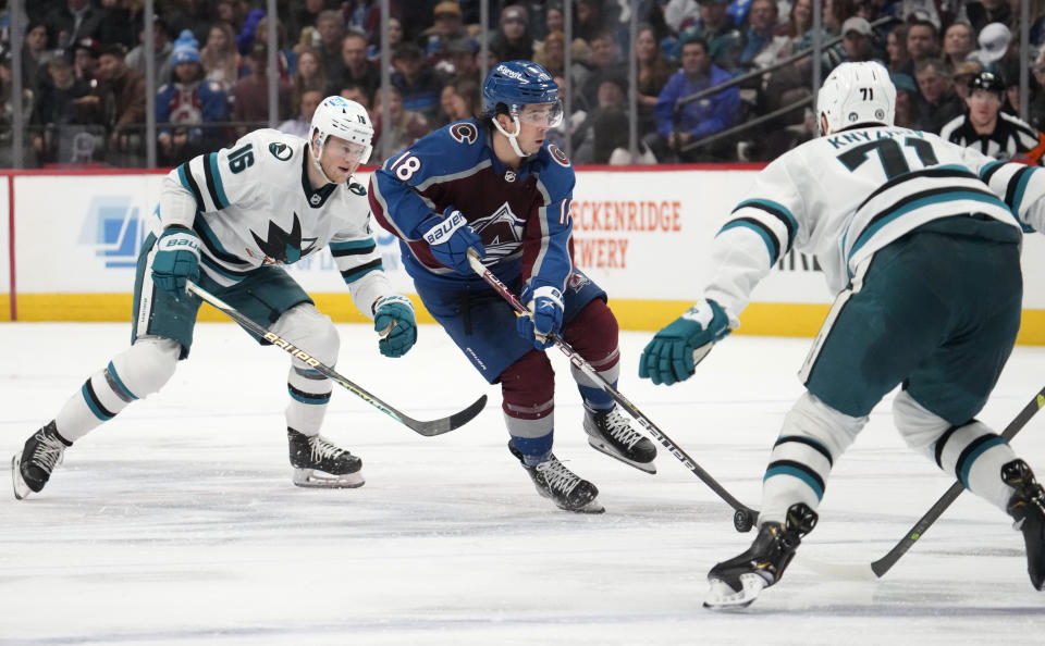 Colorado Avalanche center Alex Newhook, middle, picks up a loose puck between San Jose Sharks center Steven Lorentz, back, and defenseman Nikolai Knyzhov in the third period of an NHL hockey game Tuesday, March 7, 2023, in Denver. (AP Photo/David Zalubowski)