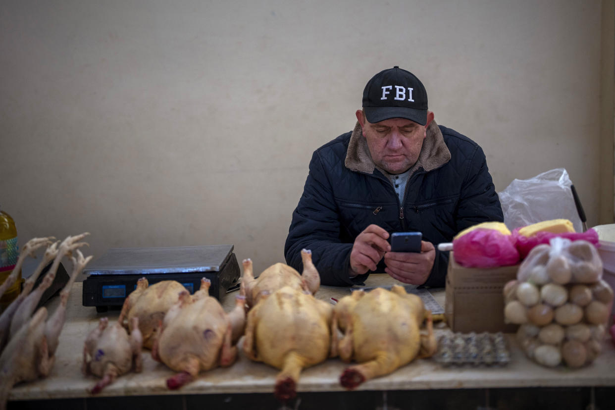A vendor looks at his phone as he waits for customers at his butcher's shop in the central market of Odessa, Ukraine, Friday, Feb. 18, 2022. (AP Photo/Emilio Morenatti)