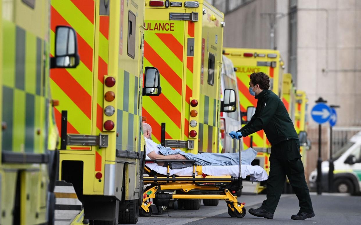 Ambulance staff pushes a bed with an patient outside the Royal London hospital in London - Shutterstock