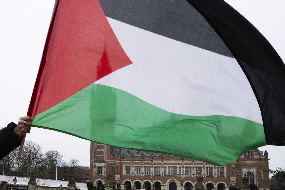 A demonstrator waves the Palestinian flag outside the United Nations' highest court, rear, during historic hearings in The Hague, Netherlands, Wednesday, Feb. 21, 2024, into the legality of Israel's 57-year occupation of the West Bank and east Jerusalem, plunging the 15 international judges back into the heart of the decades-long Israeli-Palestinian conflict. Six days of hearings at the International Court of Justice, during which an unprecedented number of countries will participate in proceedings, are scheduled as Israel continues its devastating assault on Gaza. (AP Photo/Peter Dejong)