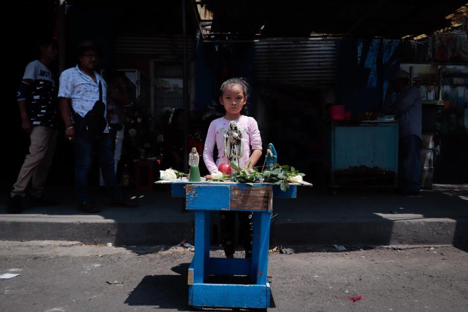 A girl stands behind an altar with roses, an apple and a figure in honour of the Holy Death to ask him to protect her family in Mexico.