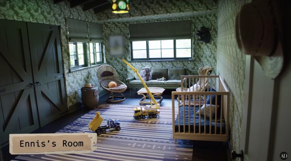 A room with green barn doors, green wallpaper with prints of wolves, a wooden crib and green couch