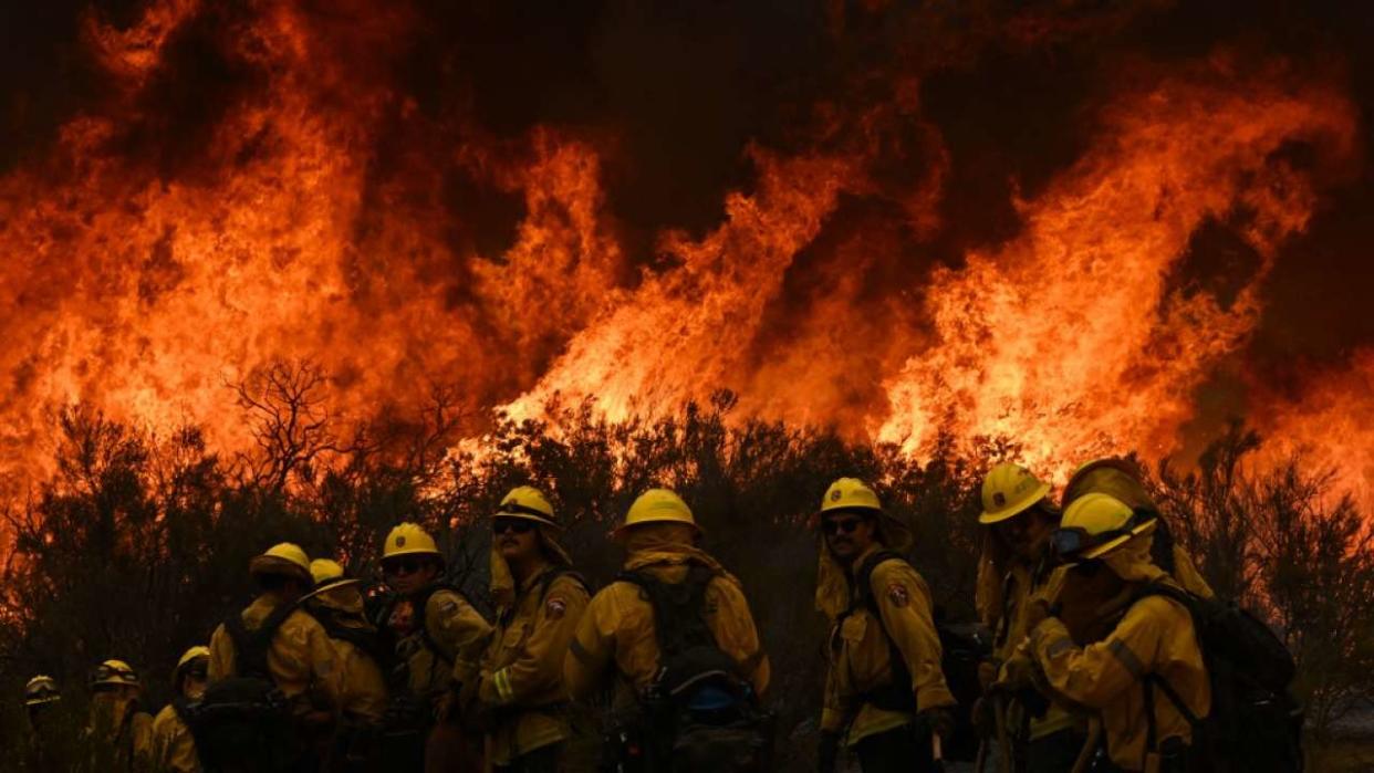 CalFire firefighters turn away from the fire to watch for any stray embers during a firing operation to build a line to contain the Fairview Fire near Hemet, California, on September 8, 2022. - A ferocious heat wave scorching the western United States could finally begin to wane in the coming days, forecasters said on September 7, but they warned of dangerous fire conditions as howling winds sweep through the bone-dry region. (Photo by Patrick T. FALLON / AFP)