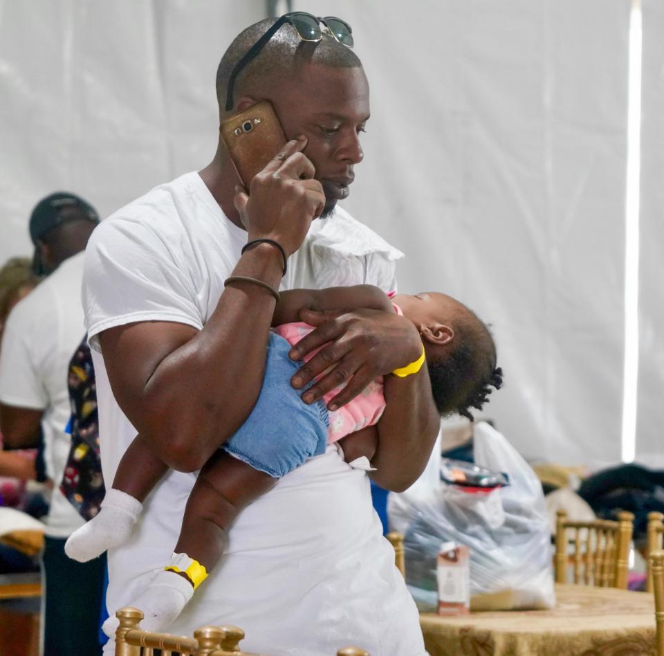 Hurricane Dorian evacuee Cecil Grant, 31, cradles his sleeping daughter, Yalissa, 7 months, while he makes a phone call at a shelter in Nassau, Bahamas, a day after fleeing their longtime home on Abaco after the storm destroyed their house and much of the surrounding community.