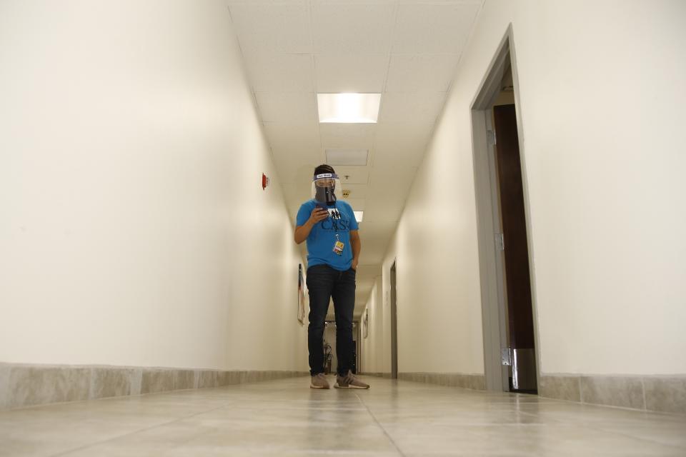 Wearing a face covering and face shield while working due to the coronavirus, Maico Olivares, lead voter registration organizer for Central Arizonans for a Sustainable Economy, works his phone as he tries to reach about 25 people a day, mostly within the Latino community, to persuade them to register to vote Thursday, Aug. 6, 2020, in Phoenix. Like others who register people to vote, those efforts have become extremely difficult during the pandemic. (AP Photo/Ross D. Franklin)