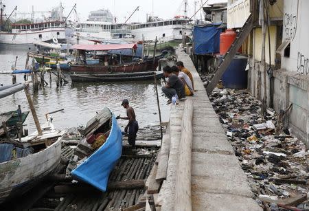 A man paints a boat on a makeshift dry dock next to the seawall protecting Luar Batang, one of the oldest kampongs in Jakarta, dating back to the16th century, in north Jakarta October 7, 2014. REUTERS/Darren Whiteside