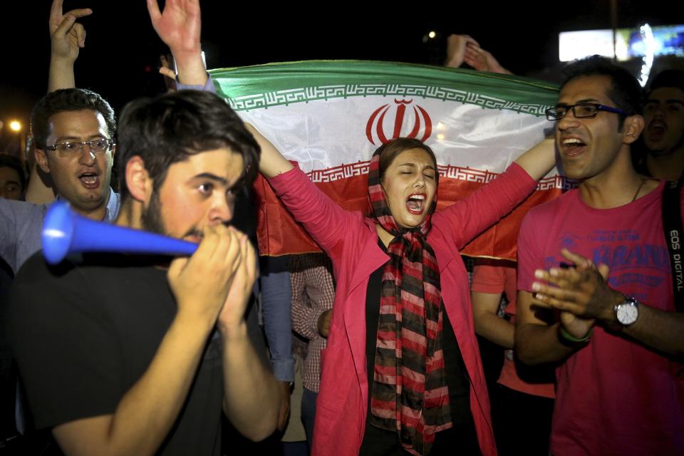 FILE - In this July 14, 2015 file photo, an Iranian woman holds up a national flag as people celebrate a landmark nuclear deal, in Tehran, Iran. The race for the White House could mean another four years of President Donald Trump’s “maximum pressure” campaign of crippling sanctions. Or it could bring Joe Biden, who has raised the possibility of the U.S. returning to Iran’s 2015 nuclear deal with world powers. (AP Photo/Ebrahim Noroozi, File)