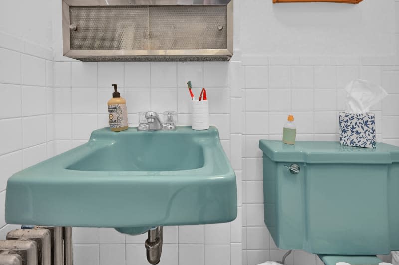 A bathroom with white tile and teal sink and toilet.