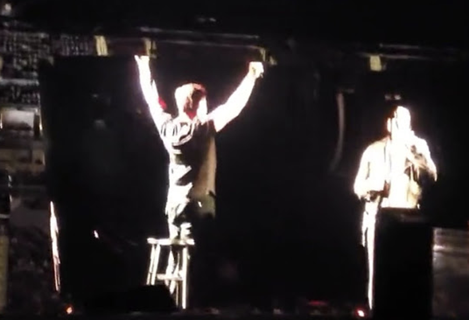 Elon Musk, with arms aloft, joined Dave Chappelle onstage at the Chase Center in San Francisco on Sunday (Jean Wilda / YouTube (screengrab))