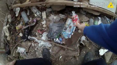 A still image captured from police body camera video appears to show a Baltimore police officer placing a small plastic bag in a trash-strewn yard as two colleagues look on (not shown) according to the Maryland Office of the Public Defender in this image released in Baltimore, Maryland, U.S. on July 19, 2017. Courtesy Baltimore Police Department/Handout via REUTERS