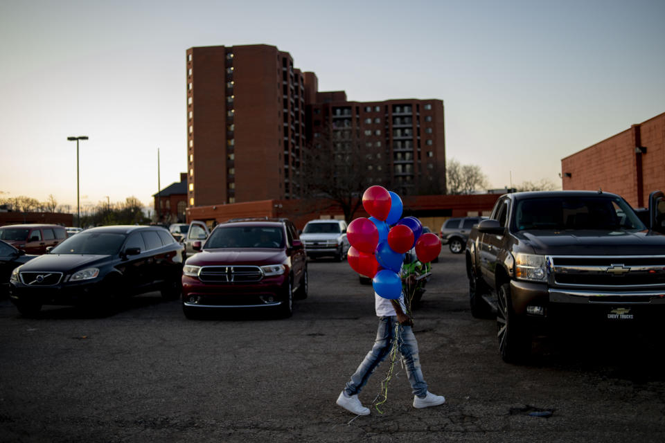 In this Sunday, May 3, 2020, photo, a Flint man walks with a bundle of balloons as he arrives to commemorate the life of Calvin Munerlyn during a vigil in Flint, Mich. A woman, her adult son and husband have been charged in the fatal shooting of Munerlyn, a security guard who refused to let her daughter enter a Family Dollar in Michigan because she wasn't wearing a face mask to protect against transmission of the coronavirus. (Jake May/The Flint Journal-MLive.com via AP)