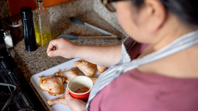 woman seasoning chicken in kitchen