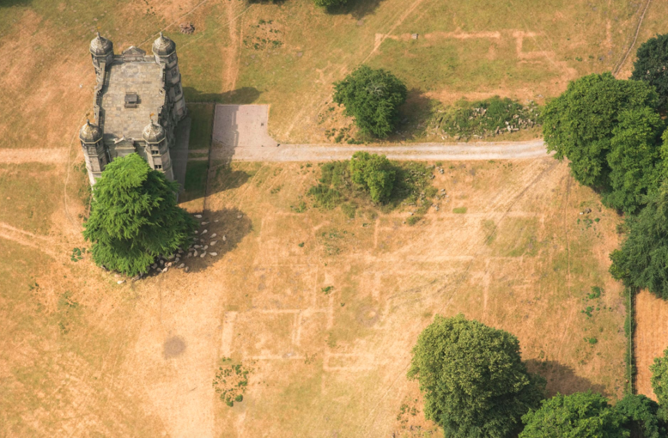 <p>The large building on the left is a gatehouse built in 1557, during the reign of Elizabeth I, while the lighter lines in the centre are where the dying grass has revealed the buried foundations of Tixall Hall in Staffordshire (Historic England) </p>