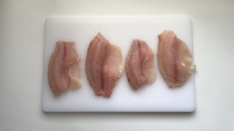 raw tilapia fillets on cutting board