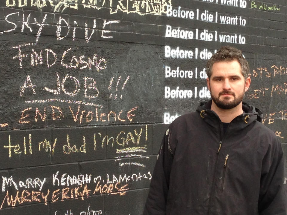 In this Nov. 7, 2013 photo, Rick Destito poses near the “Before I Die” wall he painted on the former factory building he owns in Syracuse, N.Y. The inscription on the building invites passers-by to complete the sentence: “Before I die, I want to...” The phenomenon became global since artist Candy Chang created the first wall on an abandoned house in her New Orleans neighborhood in 2011. More than 400 walls have gone up in the United States as well as 60 other countries. (AP Photo/Carolyn Thompson)