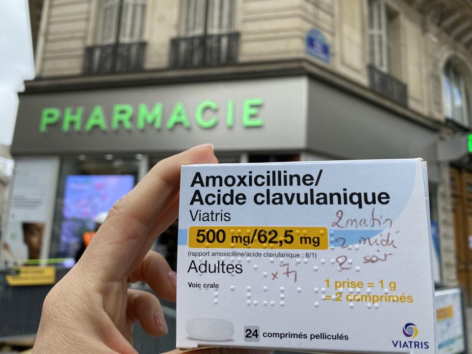 The author holding up a box of pills with neat French writing on the front while standing in front of a pharmacy