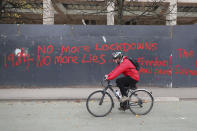 A man cycles past anti-lockdown graffiti in Manchester, England, Monday, Oct. 19, 2020 as the row over Greater Manchester region's coronavirus status continues. Britain’s government says discussions about implementing stricter restrictions in Greater Manchester must be completed Monday because the public health threat caused by rising COVID-19 infections is serious and getting worse. (Peter Byrne/PA via AP)