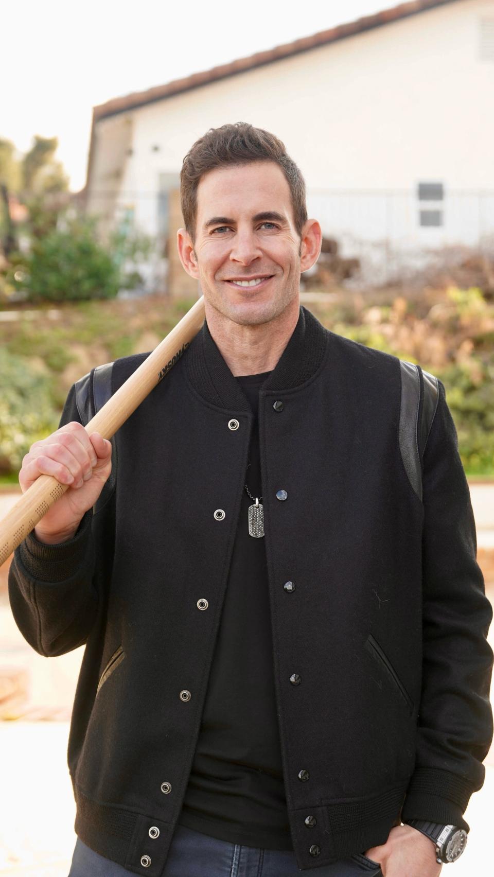 Tarek El Moussa smiles with a tool hanging over his shoulder.