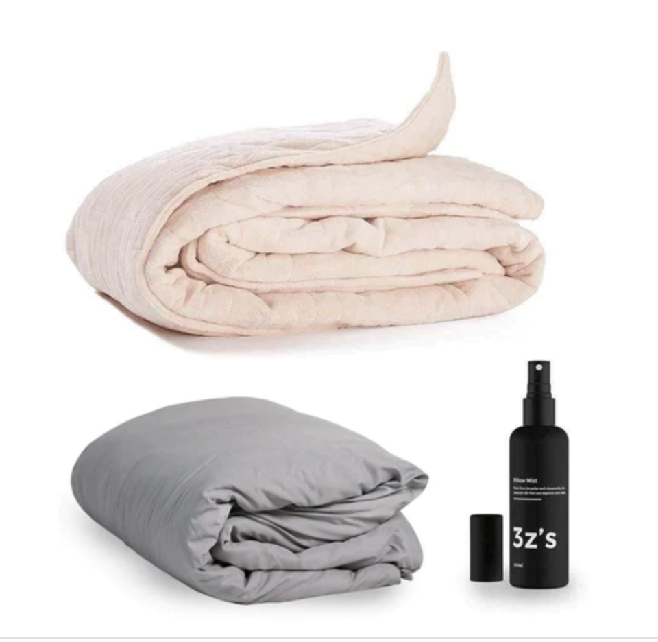 Two calming blankets, one at the top in pink and one at the bottom in grey and a black bottle of sleep spray, all on a white background. 