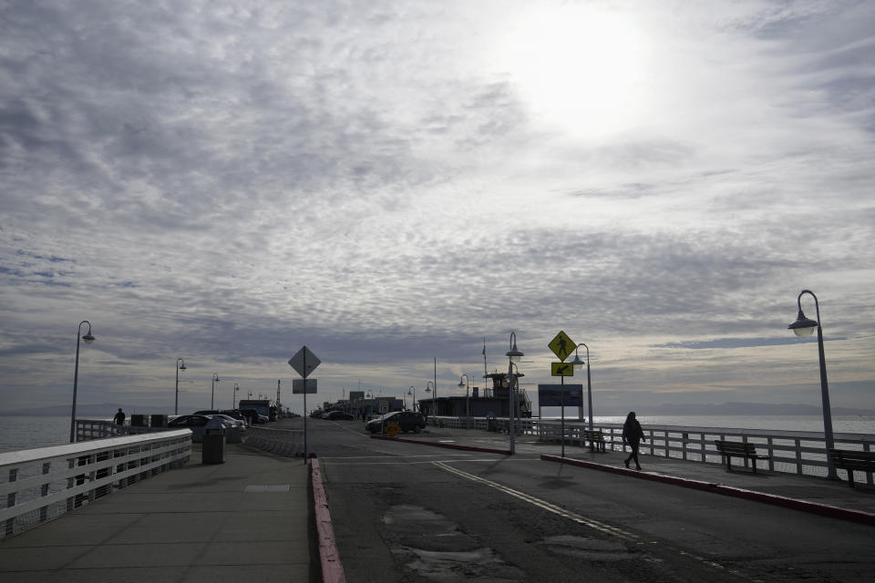 A person walks along the Santa Cruz Wharf in Santa Cruz, Calif., Friday, Jan. 12, 2024. Rising seas, frequent storms take toll on California's iconic piers, threatening beach landmarks.(AP Photo/Jeff Chiu)