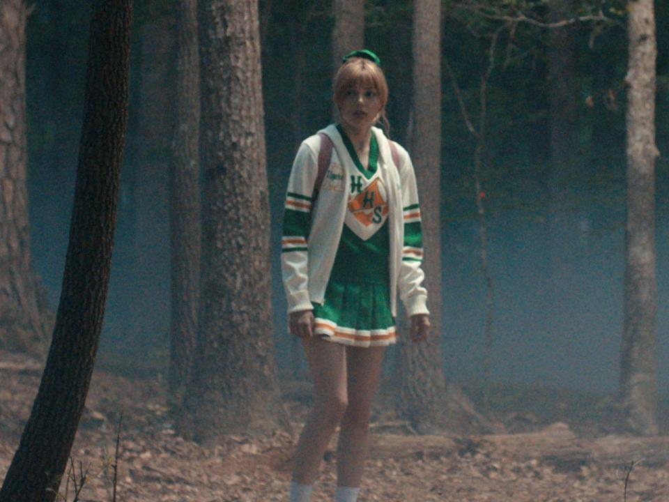 grace van dien as chrissy in stranger thigns season four, wearing a cheerleading uniform walking around alone in a forest