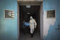 In this Sunday, Feb. 16, 2020, photo, medical workers move a person who died from COVID-19 at a hospital in Wuhan in central China's Hubei province. Chinese authorities on Monday reported a slight upturn in new virus cases and hundred more deaths for a total of thousands since the outbreak began two months ago. (Chinatopix via AP)