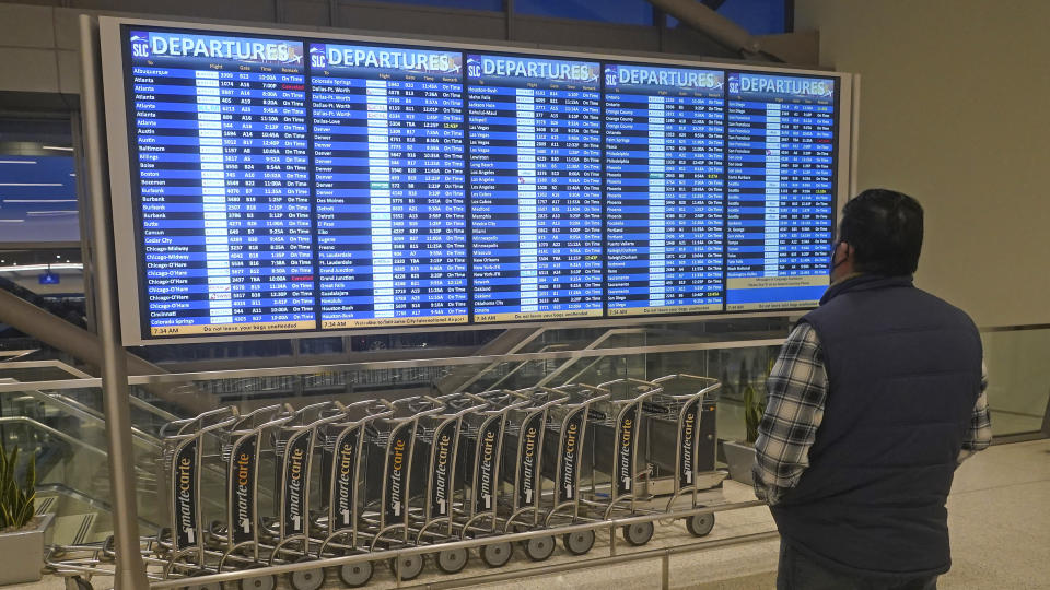 A man looks at the departures board at Salt Lake City International Airport Friday, Dec. 24, 2021, in Salt Lake City. At least three major airlines say they have canceled dozens of flights because illnesses largely tied to the omicron variant of COVID-19 have taken a toll on flight crew numbers during the busy holiday travel season. (AP Photo/Rick Bowmer)