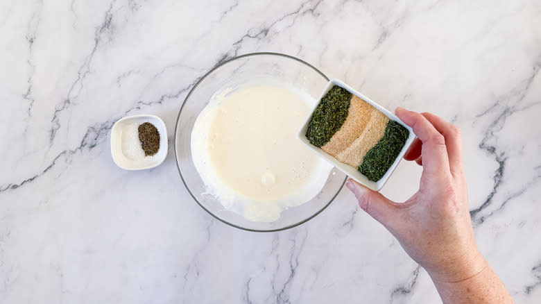 hand adding seasoning to dressing