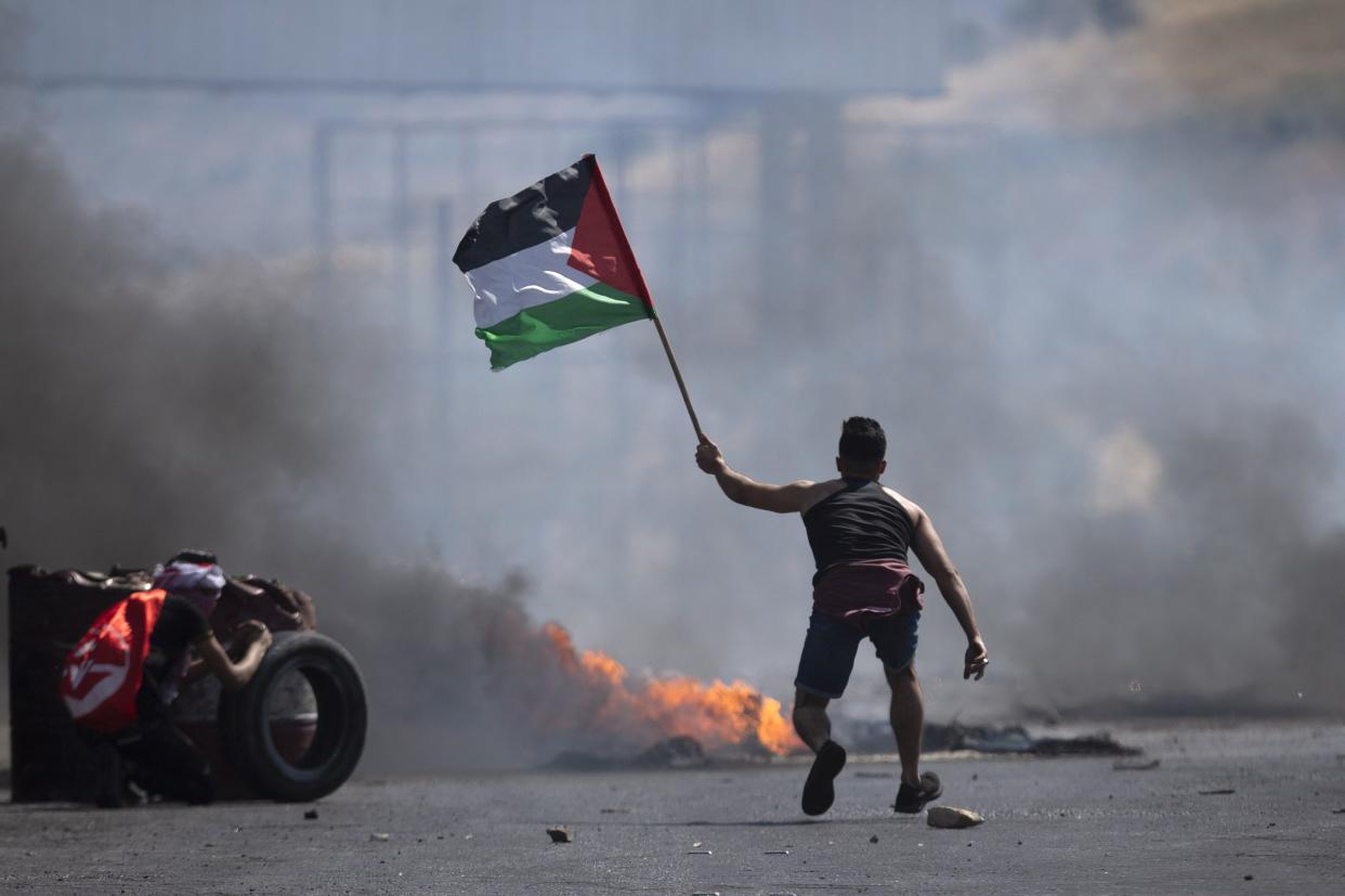 A protester waves the Palestinian flag during clashes with the Israeli forces at the Hawara checkpoint, south of the West Bank city of Nablus of Friday.