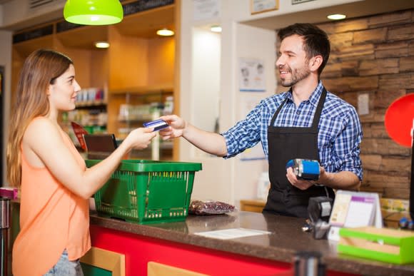 Profile view of a young woman paying with a credit card to a store clerk in a supermarket