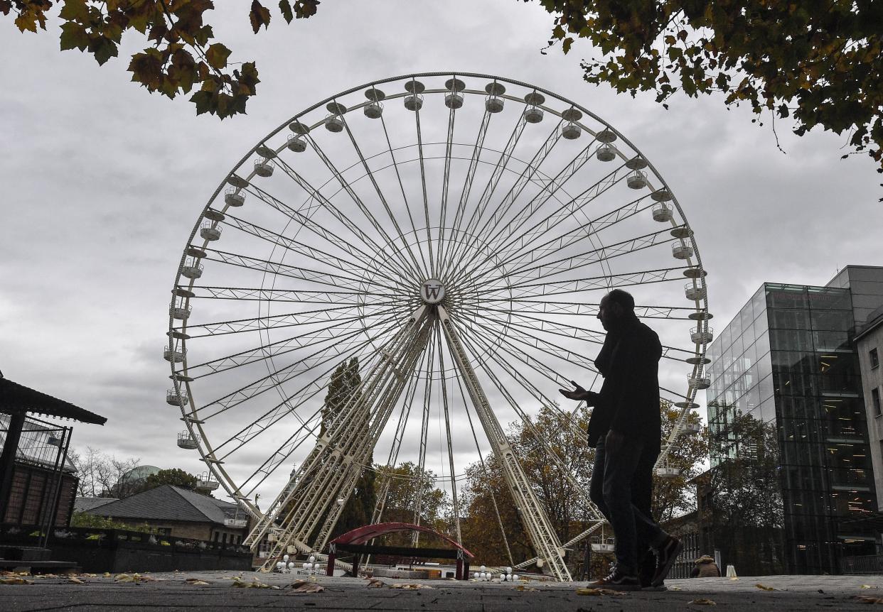 A man passes a closed ferris wheel in the city center of Essen, Germany on Monday, Nov. 2, 2020. A one-month-long partial lockdown due to the coronavirus pandemic becomes effective in Germany on Monday.