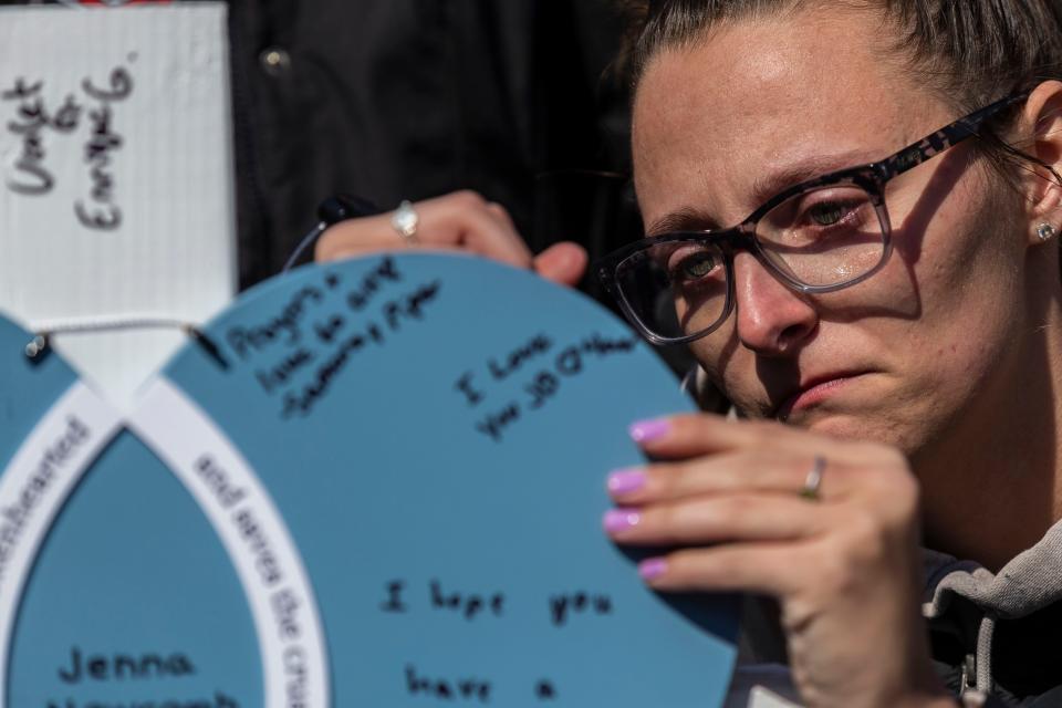 Rockford East High softball coach Madi Hecox cries as she signs Jenna Newcomb's memorial cross during a vigil held Thursday, March 28, 2024, along Charles Street in Rockford. Newcomb was a member of the E-Rabs softball team who died Wednesday while protecting a friend and her sister during a string of violent attacks on residents of a Rockford neighborhood.