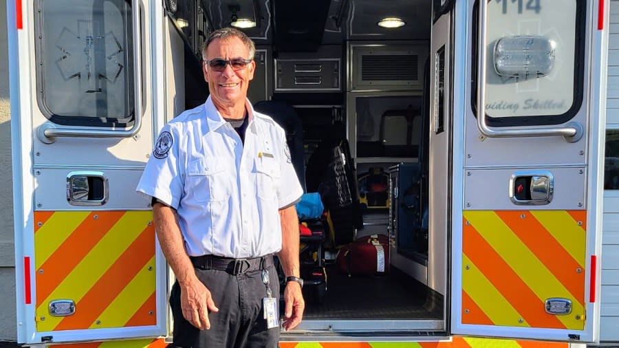 A man in paramedic uniform smiles as he stands in front of an ambulance