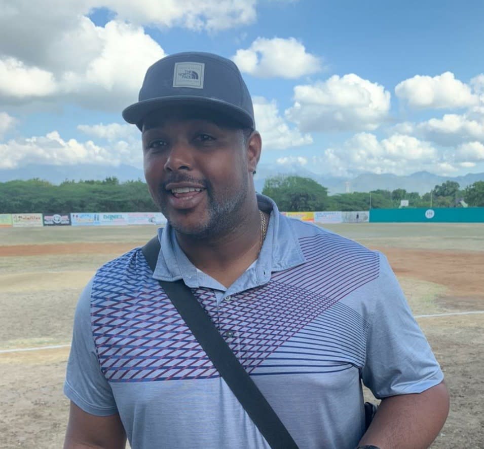 Jairo Castillo standing with a baseball field and cloud filled sky in the background.