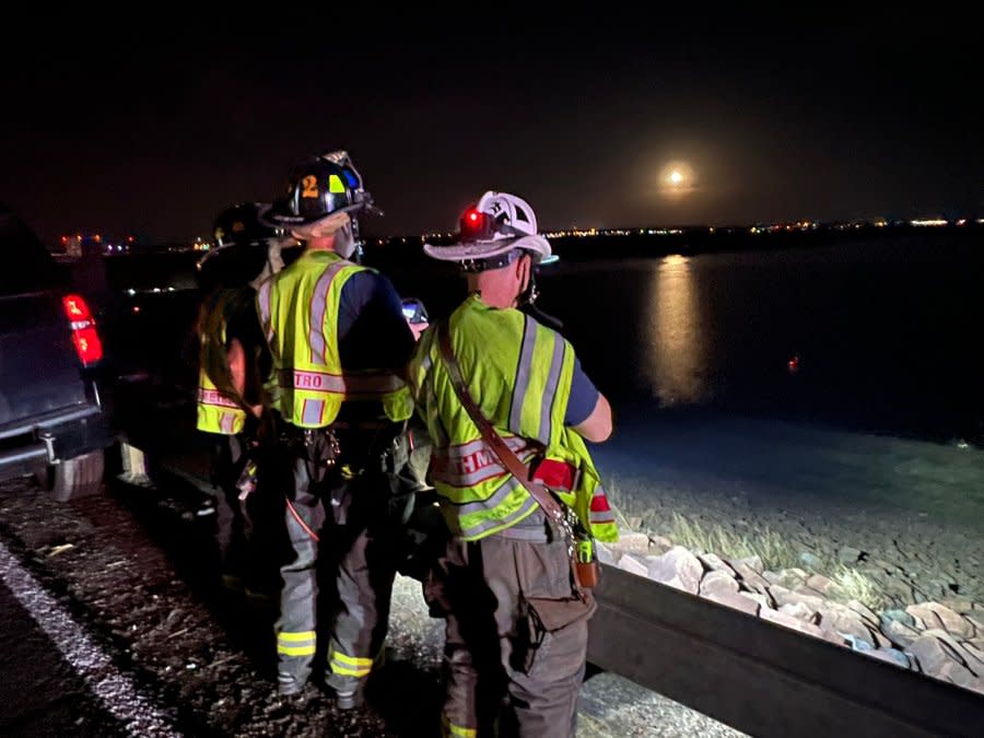 Firefighters stand next to Cherry Creek reservoir during a rescue attempt for a driver who fled their crash.