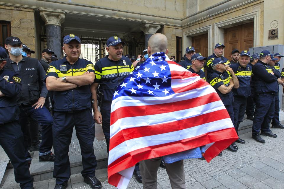 A demonstrator draped in an American flag stands in front of police during an opposition protest against the foreign influence bill at the Parliamentary building in Tbilisi, Georgia, Tuesday, May 28, 2024. (AP Photo/Shakh Aivazov)