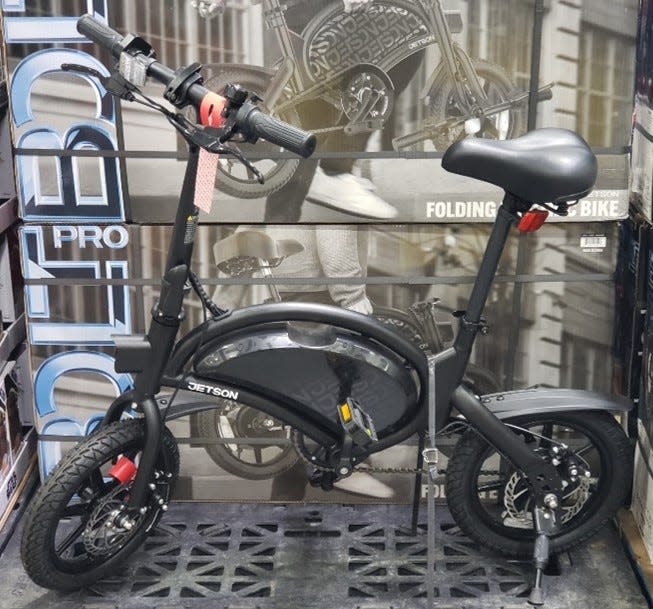 Black folding bike displayed in front of stacked boxes at Costco