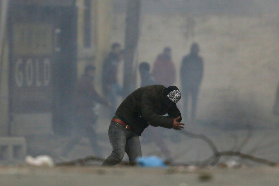 A Kashmiri protester ducks to avoid tear smoke shell during a clash with Indian paramilitary soldiers in Srinagar, Indian controlled Kashmir, Sunday, Dec. 16, 2018. A security clampdown and a strike sponsored by separatists fighting against Indian rule shut most of Indian-administered Kashmir on Sunday, a day after chaotic protests and fighting killed seven civilians and four combatants in the disputed region. (AP Photo/Mukhtar Khan)