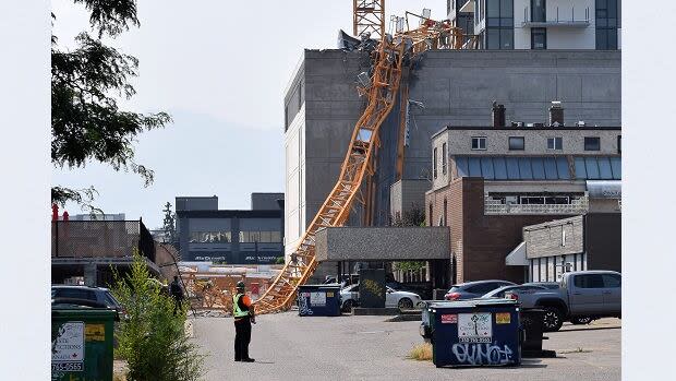 A worker looks on as a police officer investigates a collapsed crane resting on the building it damaged in Kelowna, B.C., on July 12, 2021. The crane was being used on the building site of the 25-storey Brooklyn at Bernard Block residential tower, currently under construction.