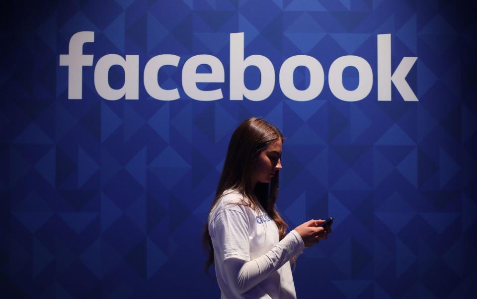 A woman using her phone underneath a Facebook sign