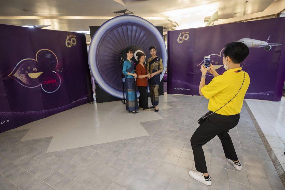 A woman poses for photos with flight attendants in a flight-themed restaurant at the Thai Airways head office in Bangkok, Thailand on Oct. 3, 2020. The airline is selling time on its flight simulators to wannabe pilots while its catering division is serving meals in a flight-themed restaurant complete with airline seats and attentive cabin crew. The airline is trying to boost staff morale, polish its image and bring in a few pennies, even as it juggles preparing to resume international flights while devising a business reorganization plan. (AP Photo/Sakchai Lalit)